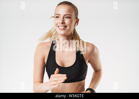 Immagine di forte donna atletico indossare tuta e sorridente in esecuzione mentre si lavora fuori isolate su muro bianco Foto Stock