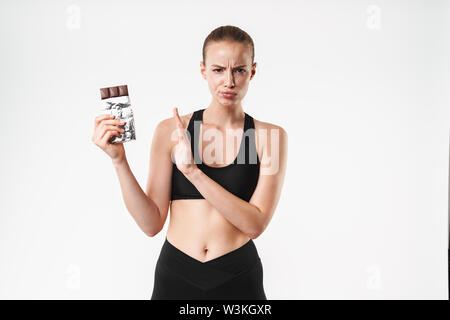 Attraente sconvolto giovani montare sportive in piedi isolato su sfondo bianco, tenendo la barra di cioccolato e mostra il gesto di arresto Foto Stock