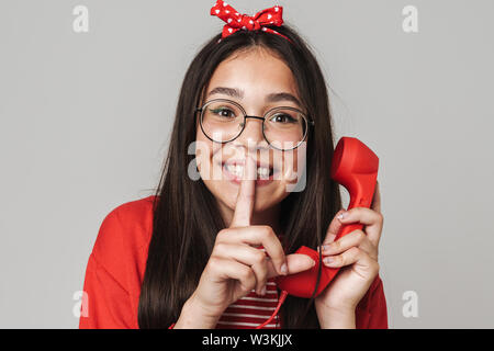 Carino felice ragazza adolescente indossare abbigliamento casual in piedi isolate su uno sfondo grigio, la chiamata sul telefono fisso Foto Stock