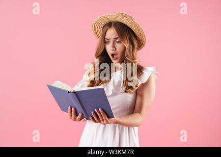 Foto di un scioccato confuso carino giovane donna graziosa posa isolato sulla parete rosa sfondo libro di lettura. Foto Stock