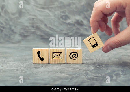 Mettendo mano blocco di legno cube con il simbolo telefono, e-mail, indirizzo e telefono cellulare. Sito web pagina contattaci o e-mail concetto di marketing Foto Stock