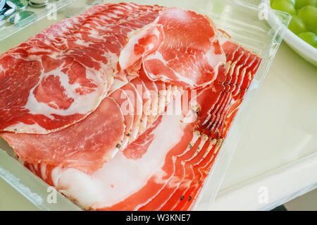 Prosciutto e aroma di spezie, tagliata a fettine sottili su un tavolo bianco con pane. close up. Foto Stock