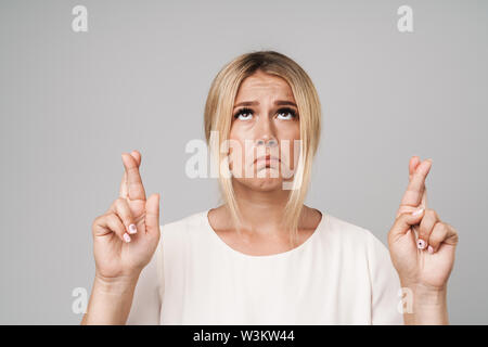 Ritratto di un attraente casual donna isolate su uno sfondo grigio, tenendo le dita incrociate per buona fortuna Foto Stock