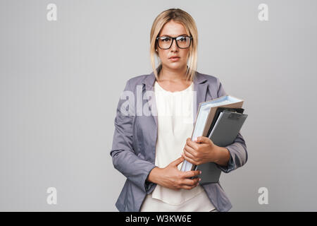 Attraente dai capelli biondi imprenditrice in giacca standing isolate su uno sfondo grigio, portando le cartelle Foto Stock