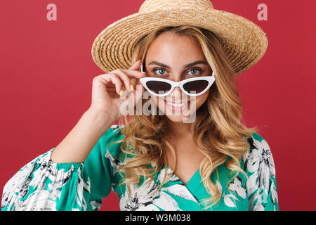 Foto di incredibile ottimista giovane biondo carino donna nel vestire in posa isolato sulla parete rossa sullo sfondo indossando occhiali da sole. Foto Stock