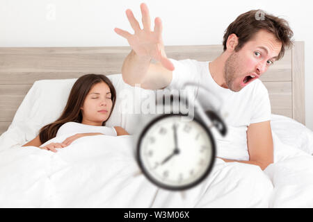 Wake up - giovane svegliarsi presto gettando sveglia. Strano concetto di letto con giovani interracial giovane svegliarsi tardi. Uomo di gettare la sveglia e donna che dorme. Femmina asiatici e caucasici modelli maschio Foto Stock