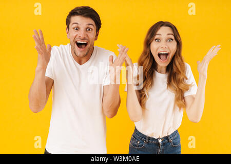 Ritratto di felice giovane uomo e donna in base t-shirt urlando e gettando le armi in telecamera isolate su sfondo giallo Foto Stock