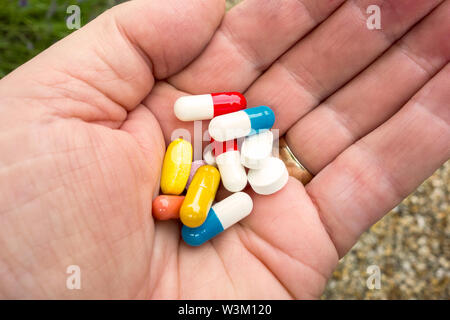Manciata di pillole: pillole medicinali e compresse in una mano d'uomo, mattina dose per una persona malata Foto Stock