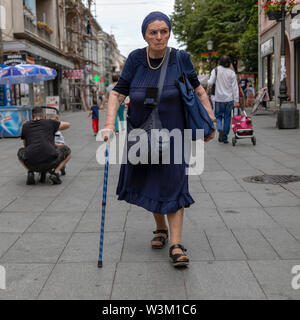 A Belgrado, in Serbia, 13 Luglio 2019: scena urbana con un senior lady camminando per la strada con bastone Foto Stock