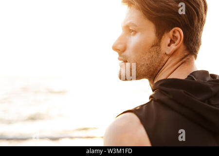 Foto di pensare maschile uomo nero che indossa la t-shirt cercando in disparte vicino al mare al mattino Foto Stock