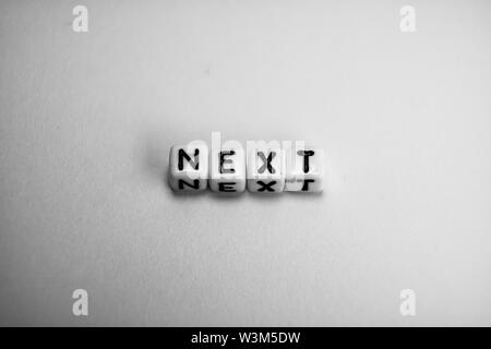 Cubi di bianco con la parola "NEXT" su carta bianca di sfondo e ombre scure Foto Stock