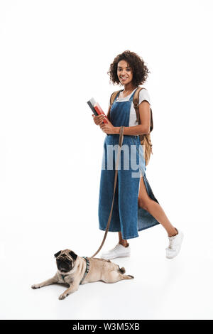 Immagine della lieta americano africano donna che indossa uno zaino con libri e poising con il suo pug isolate su sfondo bianco Foto Stock