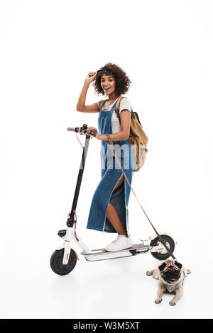 Immagine della bella african american woman in occhiali da sole poising con il suo pug e scooter isolate su sfondo bianco Foto Stock