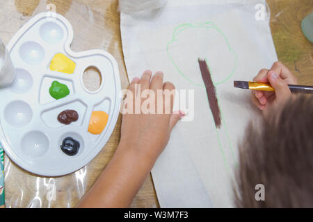 Vista superiore del bambino disegna le mani un gouache su carta. Gouache e carta per pittura e disegno del bambino. Kid mani pittura a tavola con arte materiali di consumo, Foto Stock