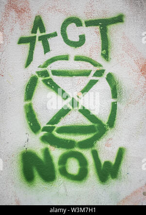 LONDON, Regno Unito - 16 luglio 2019: Graffiti di estinzione di ribellione e il logo "agire ora' Slogan su una parete durante la protesta Graffiti di estinzione della ribellione Logo Foto Stock