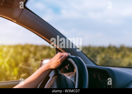 Auto di guida attraverso la campagna, femmina le mani sul volante di sterzo, close up con il fuoco selettivo Foto Stock