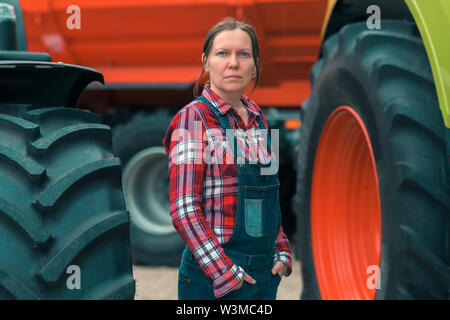 L'agricoltore femmina e il trattore. Donna facendo gli uomini del lavoro di concetto. Fattoria femmina lavoratore in posa di fronte dei macchinari agricoli. Foto Stock