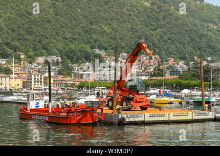 Il LAGO DI COMO, Italia - Giugno 2019: Industriale barge e pontoon con un sollevatore telescopico gru del trattore nel porto di Como sul Lago di Como. Foto Stock