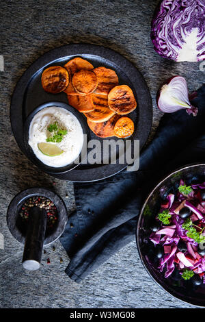 Dolce fritto fette di patate servita con panna acida dip, olive nere e insalata di cavolo rosso, cipolla rossa e barbabietole Foto Stock