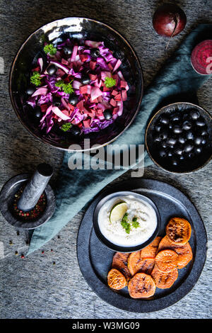 Dolce fritto fette di patate servita con panna acida dip, olive nere e insalata di cavolo rosso, cipolla rossa e barbabietole Foto Stock