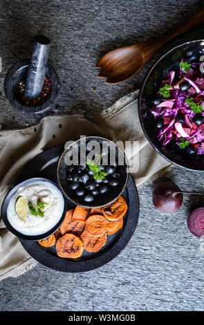 Dolce fritto fette di patate servita con panna acida dip, olive nere e insalata di cavolo rosso, cipolla rossa e barbabietole Foto Stock