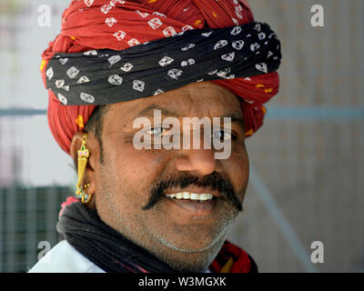 In sovrappeso di Rajasthani indiano uomo con golden orecchini tradizionale indossa un turbante di Rajasthani (pagari) e sorrisi per la fotocamera. Foto Stock