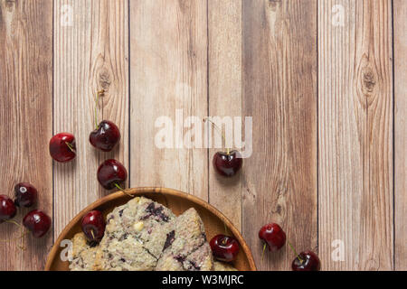 Confine con piastra in legno di ciliegio e il cioccolato bianco scones su un tavolo di legno sfondo con ciliegie fresche Foto Stock