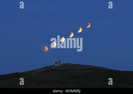 Beachy Head, UK. 16 lug 2019. Regno Unito meteo. Immagine composita mostra questa sera la luna piena eclissi parziale crescente dietro belle Tout faro in East Sussex,UK.Credit: Ed Brown/Alamy Live News Foto Stock