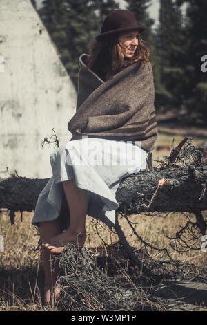 Un attraente giovane donna siede su un log avvolto in una coperta di lana. Yukon Territory, Canada Foto Stock