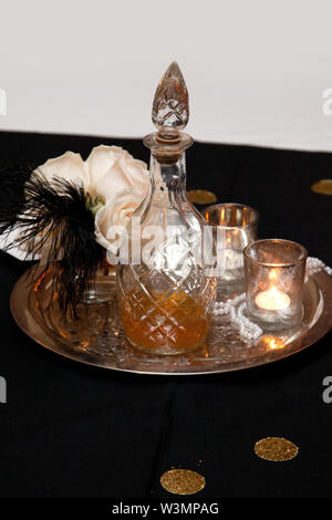 Bicchiere old fashioned liquor decanter con candele, fiori e decorazioni di piume sulla parte superiore di una tavola Foto Stock