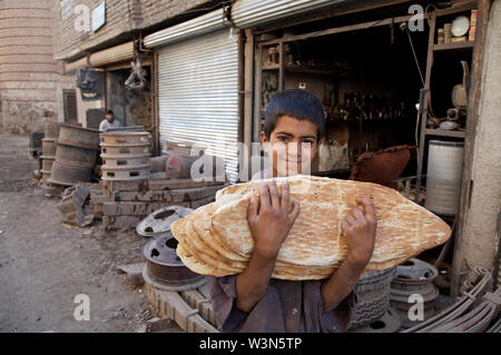 Un ragazzo afgano che lavora come un helper in un auto officina, trasporta il pane appena sfornato per i suoi colleghi, nella pia Minara quartiere di nord-ovest della città di Herat. La media uomo afgano lotte per sostenere la sua famiglia su equivalente a US $ 3 al giorno e alcune 20-30 per cento dei bambini della scuola primaria di lavoro di età per integrare il reddito familiare. Ci sono migliaia di bambini che lavorano in condizioni di rischio in tutto l'Afghanistan. Giugno 20, 2007. Foto Stock