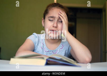 Torturato ragazza bambino legge un libro a tavola e lei è molto stanco e vuole dormire, sbadigli, si addormenta durante la lettura di storie e di lezioni Foto Stock