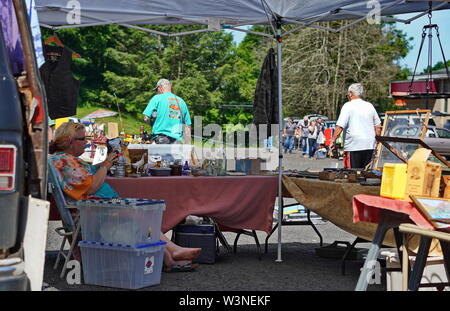 Durham, CT / STATI UNITI D'America - 24 Giugno 2019: Femmina venditore in un mercato delle pulci rilassa e orologi la sua mercanzia sotto l'ombra Foto Stock