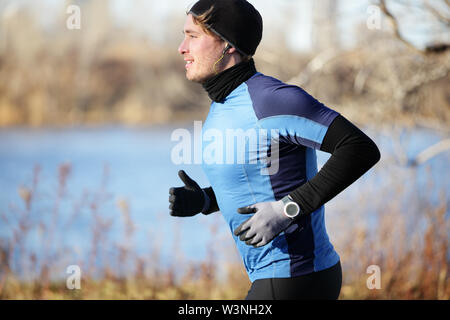 Runner uomo in autunno in esecuzione in autunno indossando i guanti e hat ascoltando musica in cuffia. Montare atleta maschio di formazione al di fuori in condizioni climatiche fredde in guide caldo capo d'abbigliamento. Modello di fitness. Foto Stock