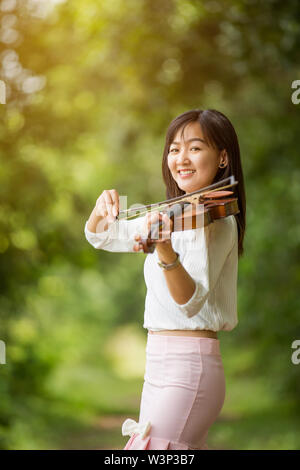 Asia donna suona il violino in giardino con il sole Foto Stock
