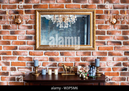 Foto del caminetto in legno con decorazioni e specchio sulla parete di mattoni dello sfondo. Foto Stock