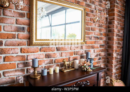 Foto del caminetto in legno con decorazioni e specchio sulla parete di mattoni dello sfondo. Foto Stock