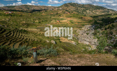 Ricefields e tradizionale Betsileo case sul Madagascar highlands, vicino ad Ambositra, sulla principale N7 road. Old Lady trasportare il legno sul suo capo. Foto Stock