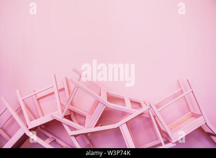 Molte sedie rosa capovolto contro lo sfondo di una parete rosa Foto Stock