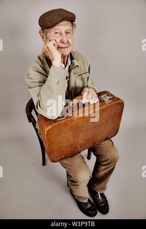 Senior si siede con la vecchia valigia su una sedia, immagine simbolica lasciando, desiderio, studio shot, Germania Foto Stock