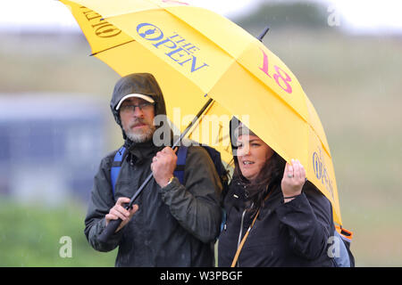 Gli spettatori si rifugiano sotto il loro ombrello durante l'anteprima giorno quattro del Campionato Open 2019 presso il Royal Portrush Golf Club. Foto Stock