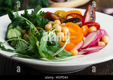 Vegano sano ciotola. Veggie ceci con insalata di verdure fresche, coloratissimo mix di pomodori ciliegini, rucola, ravanelli Cetrioli su un tavolo di legno, impianti ba Foto Stock