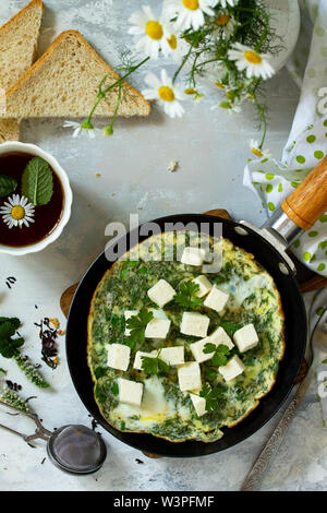 La colazione dello sfondo. Uova fritte con spinaci, formaggio feta sul tavolo di pietra. Vista superiore piatta sullo sfondo dei laici. Foto Stock