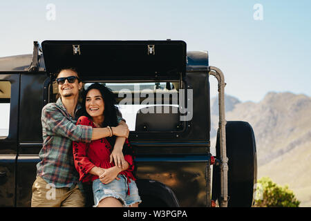 Matura in piedi accanto a loro auto in autostrada. Uomo che abbraccia la sua donna in piedi all'aperto e guardando lontano sorridente. Foto Stock