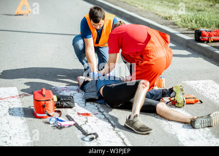 Lavoratori Ambluence applicando cura di emergenza per i feriti il sanguinamento uomo disteso sul passaggio pedonale dopo l'incidente stradale Foto Stock