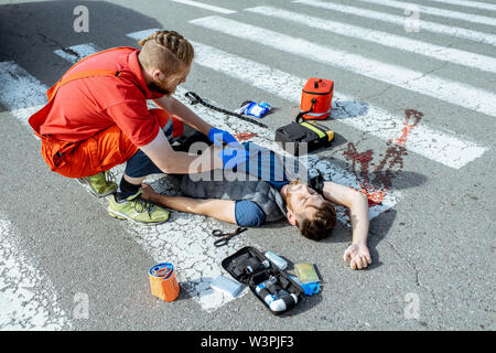 Lavoratore Ambluence applicando cura di emergenza per i feriti il sanguinamento uomo disteso sul passaggio pedonale dopo l'incidente stradale Foto Stock