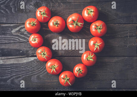 Forma di cuore formato con appena raccolto pomodori in scuro legno rustico sfondo. Spazio di copia Foto Stock
