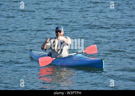 Un vero pescatore felice con catturato piccoli bassi sul suo colore blu kayak sul lago chiara Clearlake California USA America sulla tranquilla giornata di sole in estate da se stesso Foto Stock