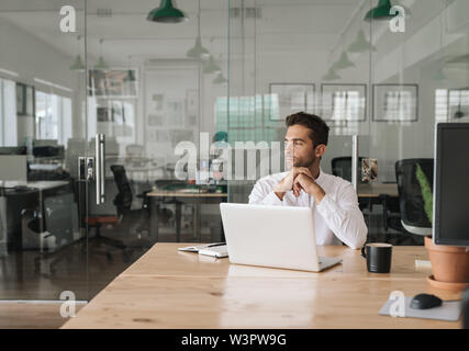 Giovane imprenditore nel profondo pensiero mentre è seduto in un ufficio Foto Stock