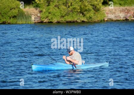 Un vero pescatore felice con catturato piccoli bassi sul suo colore blu kayak sul lago chiara Clearlake California USA America sulla tranquilla giornata di sole in estate da se stesso Foto Stock